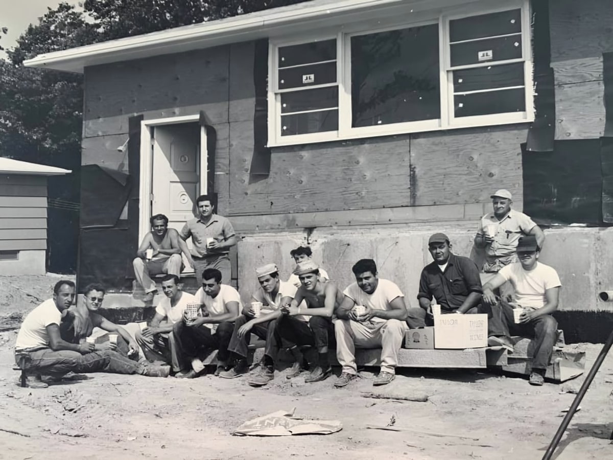 Vintage black-and-white photo of workers seated outside a house under construction