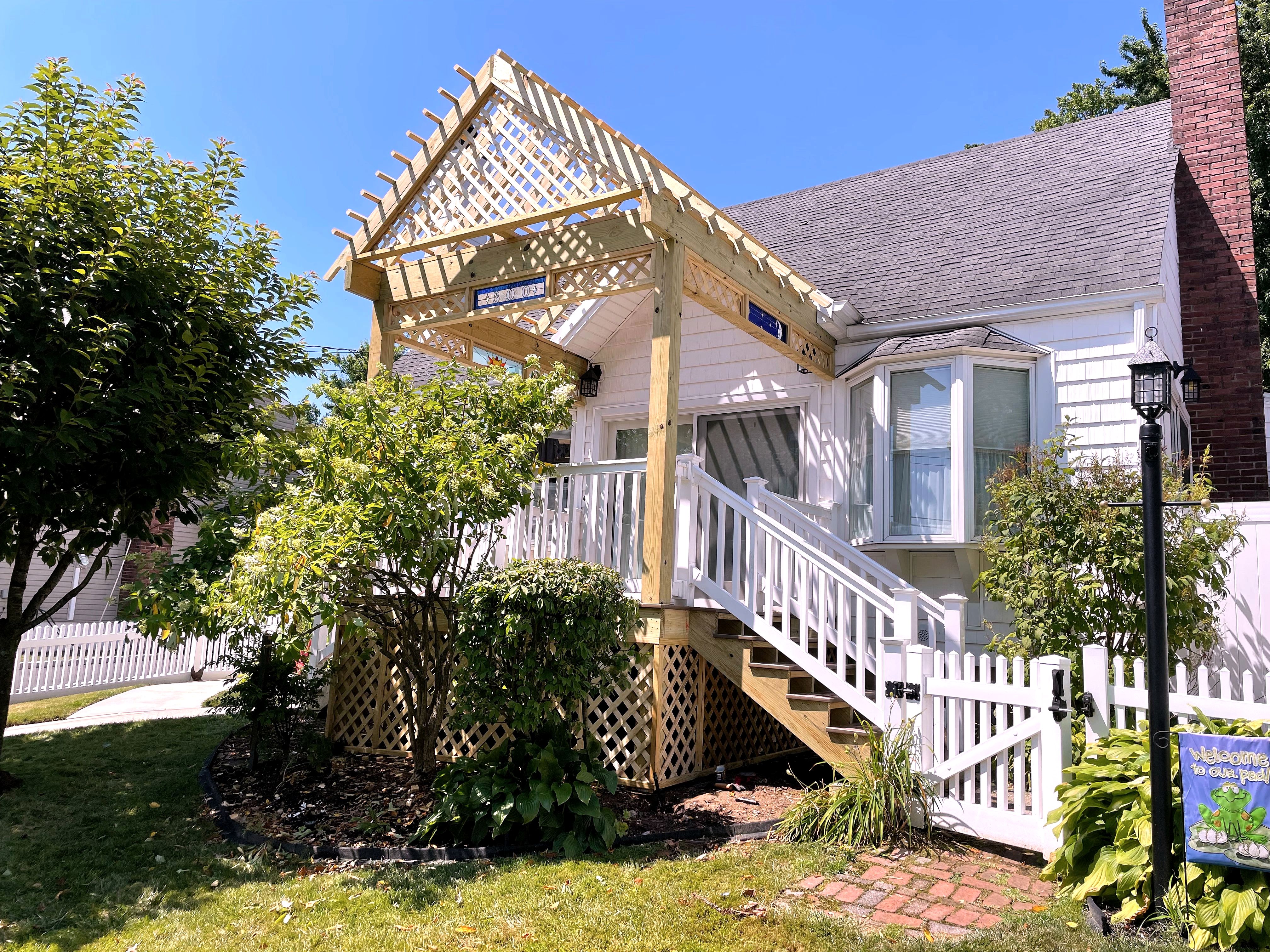 Wooden pergola-topped entry staircase on white house with lattice skirting